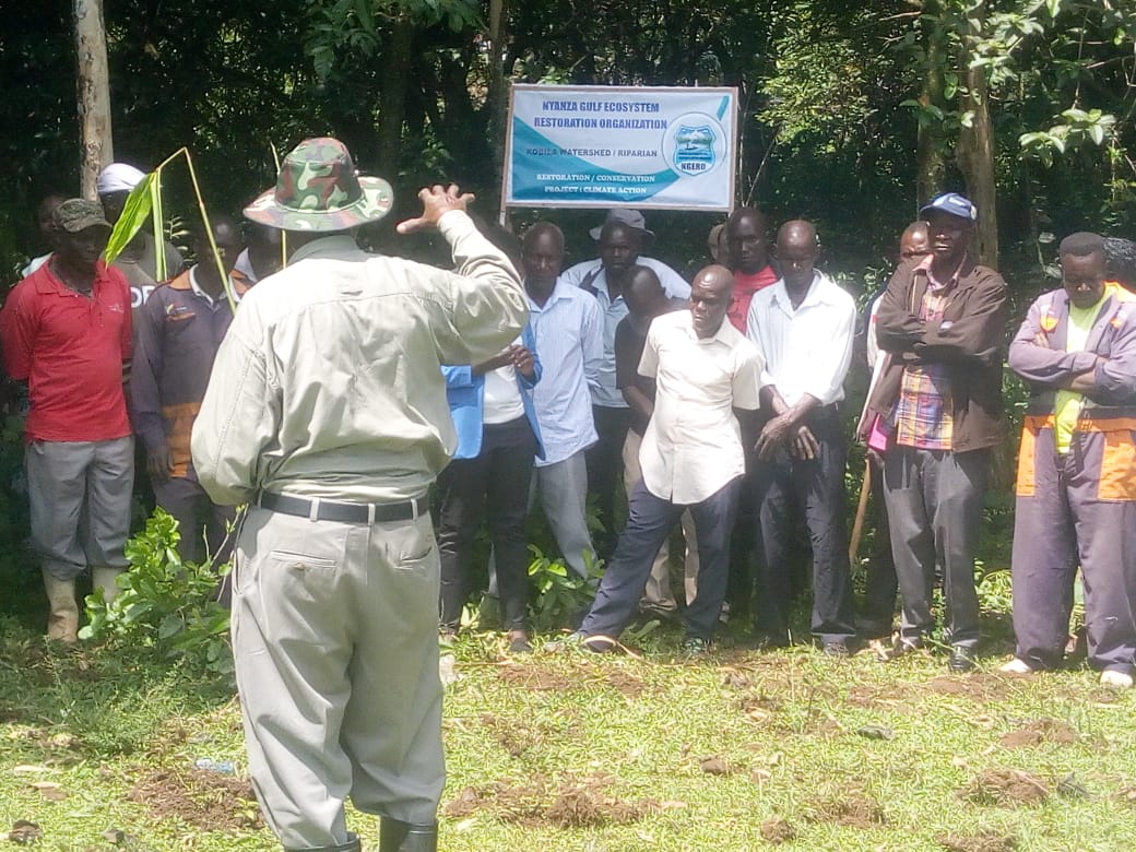 NGERO field officer addressing residents beside the project banner